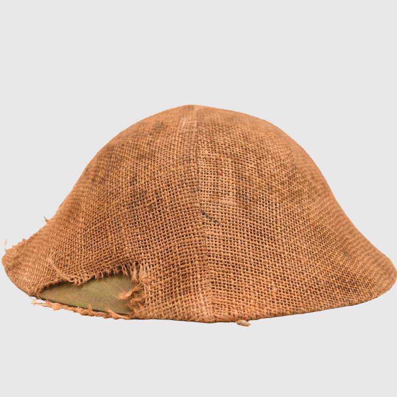 BRITISH WWI VERY FIRST PATTERN BRODIE HELMET IN GREEN WITH BATTLE DAMAGE AND FIELD COVER.