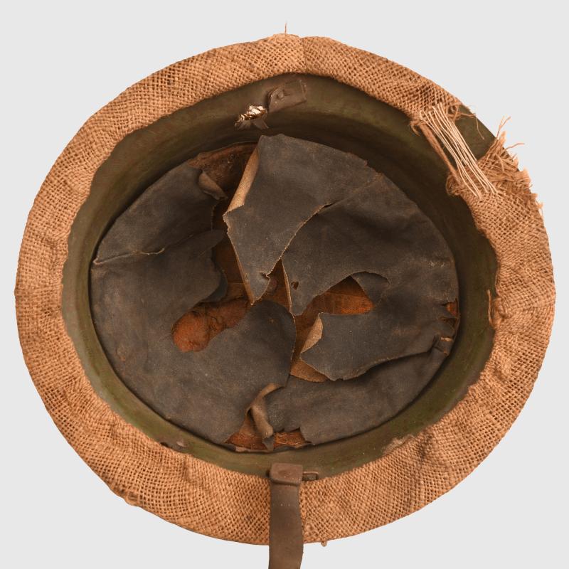 BRITISH WWI VERY FIRST PATTERN BRODIE HELMET IN GREEN WITH BATTLE DAMAGE AND FIELD COVER.