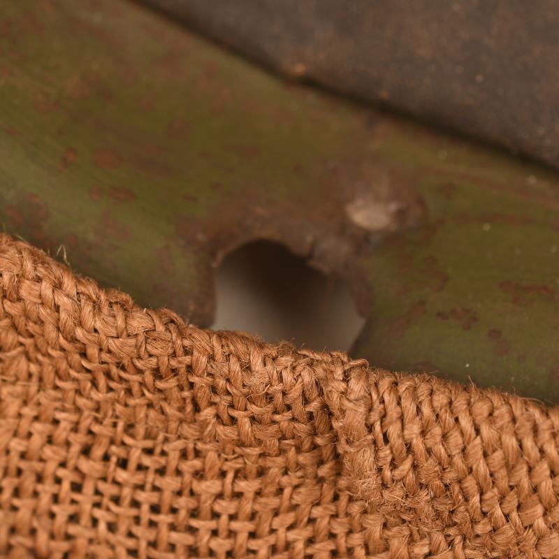 BRITISH WWI VERY FIRST PATTERN BRODIE HELMET IN GREEN WITH BATTLE DAMAGE AND FIELD COVER.